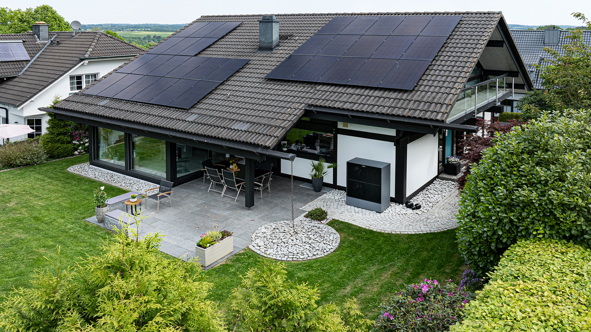 dew21-magazin-private-photovoltaikanlage-1920x1080 Haus mit Solarpanels auf dem Dach, Garten und möblierter Terrasse.