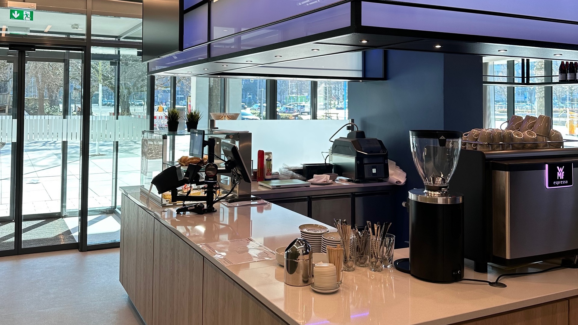 dew21-magazin-twentyone-cafe-1920x1080 Innenansicht eines modernen Cafés mit Theke, Espressomaschine und Gebäckauslage.