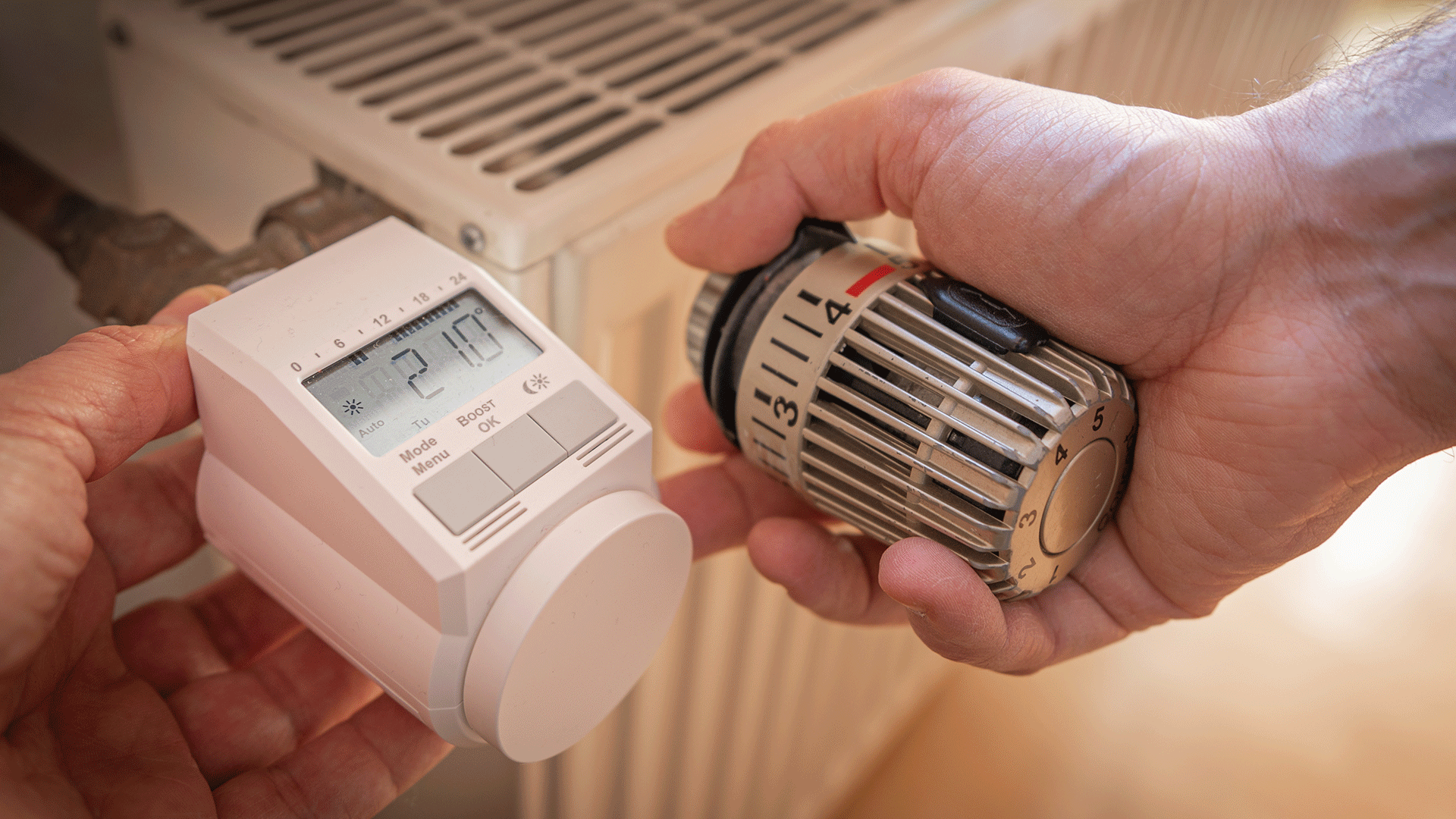 dew21-magazin-digitales-thermostate-1920x1080 Zwei Hände arbeiten an einem Heizkörper. Die linke Hand hält ein digitales Thermostat, die rechte einen herkömmlichen Regler.