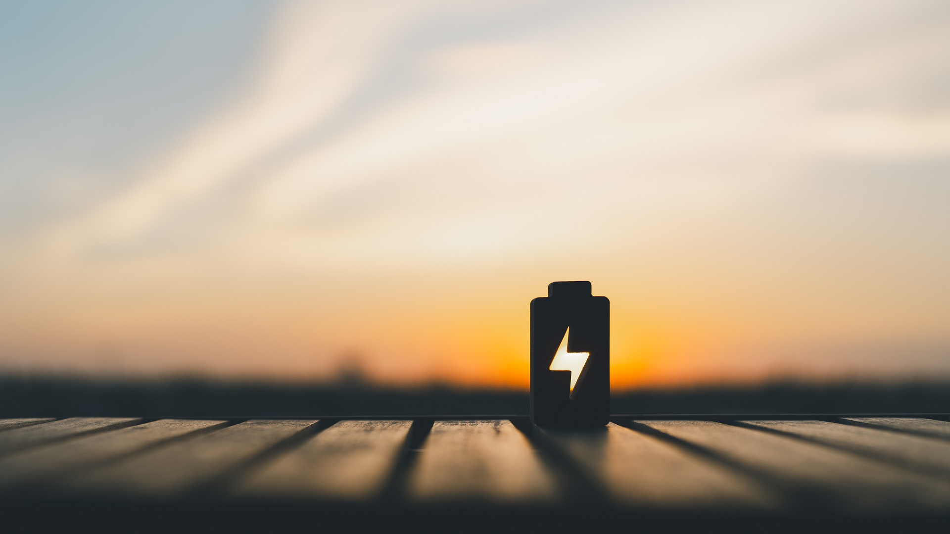 Technology battery high power electric energy with a connected charging cable. Battery to electric cars and mobile devices with clean electric, Green renewable energy battery storage future. Silhouette eines Batterie-Symbols mit Blitz auf Holzoberfläche, Hintergrund Sonnenuntergang.
