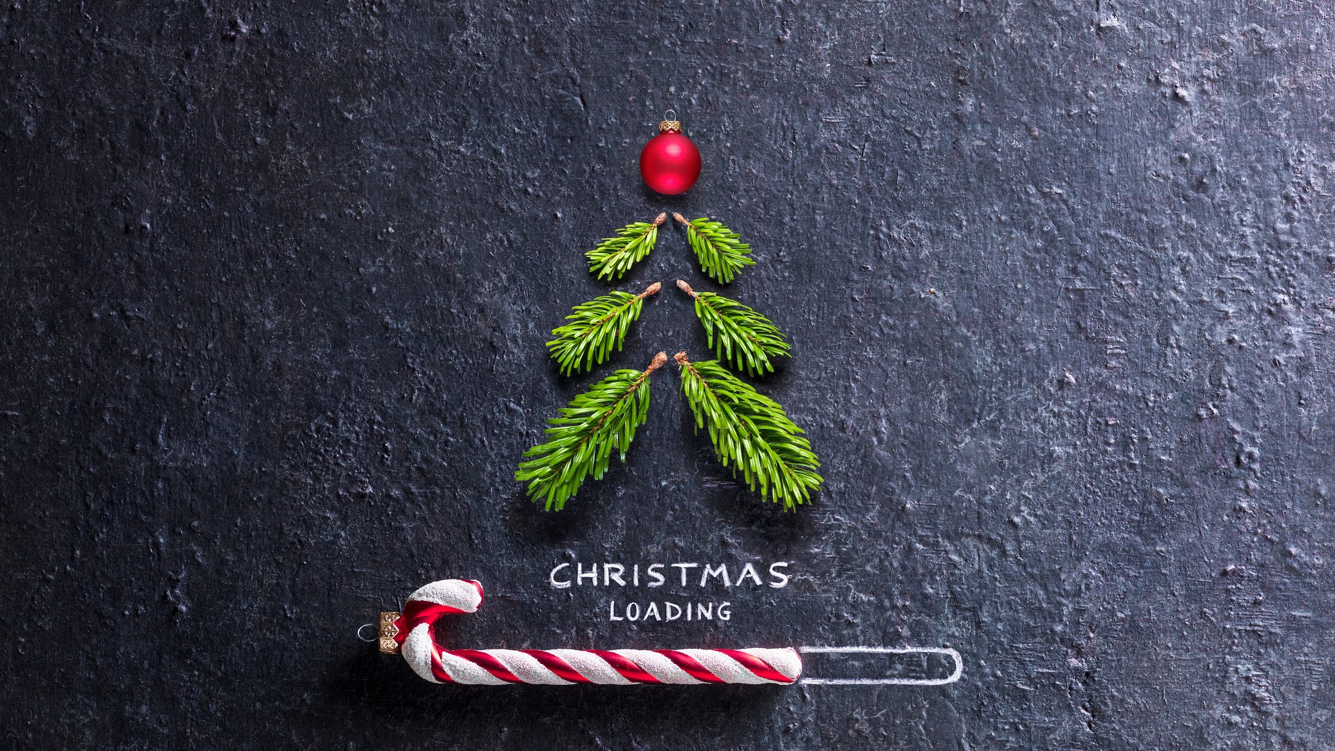 Christmas Card - Loading Concept - Tree And Candy Canes On Black Stone Weihnachtsbaum aus kleinen Zweigen und roter Kugel auf dunklem Hintergrund, darunter "CHRISTMAS LOADING" mit Zuckerstange im Ladebalken.