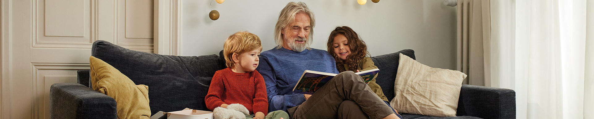 Ein Mann und 2 Kinder sitzen auf der Couch und lesen ein Buch.