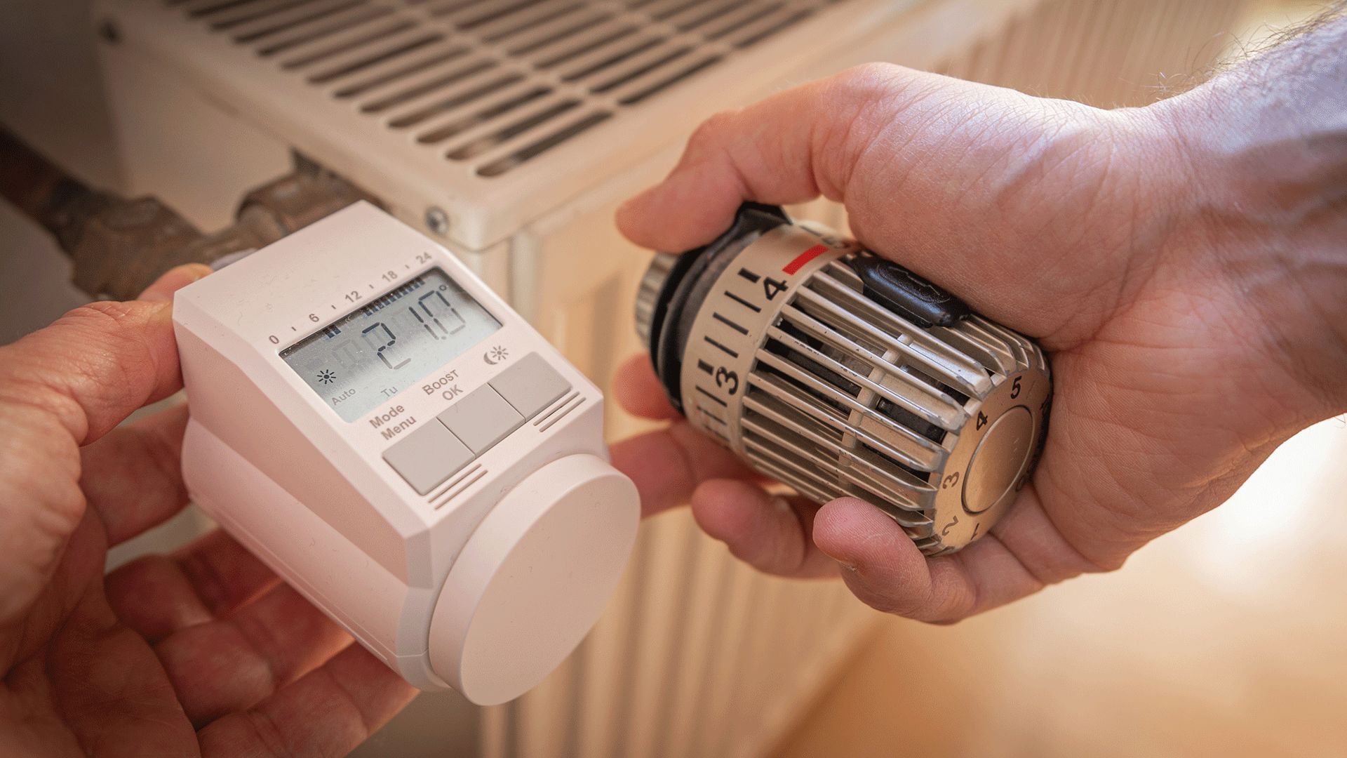 Zwei Hände arbeiten an einem Heizkörper. Die linke Hand hält ein digitales Thermostat, die rechte einen herkömmlichen Regler.