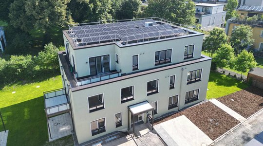 Gebäude mit Solaranlage Modernes Gebäude mit Flachdach und Solarpanels, umgeben von Grünflächen und Bäumen.