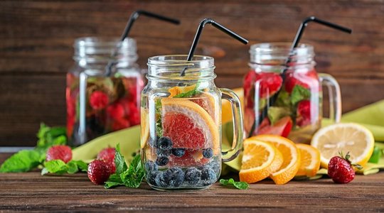 Infused Water Drei Gläser mit fruchtinfusiertem Wasser, gefüllt mit Erdbeeren, Blaubeeren, Orangen- und Zitronenscheiben sowie Minzblättern.