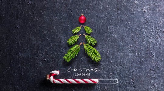 Weihnachten-Nachhaltigkeit Weihnachtsbaum aus kleinen Zweigen und roter Kugel auf dunklem Hintergrund, darunter "CHRISTMAS LOADING" mit Zuckerstange im Ladebalken.