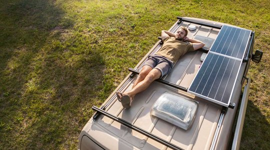 Solaranlage Mann liegt auf Wohnmobildach mit Solarpaneelen, geparkt auf grasbewachsener Fläche