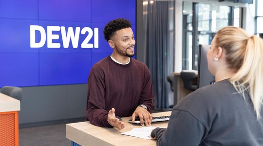 Kundenservice DEW21 Zwei Personen interagieren an einem Schalter, im Hintergrund ein Bildschirm mit "DEW21".
